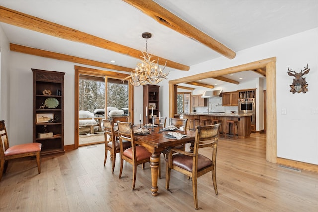 dining space with sink, beam ceiling, light hardwood / wood-style flooring, and a notable chandelier