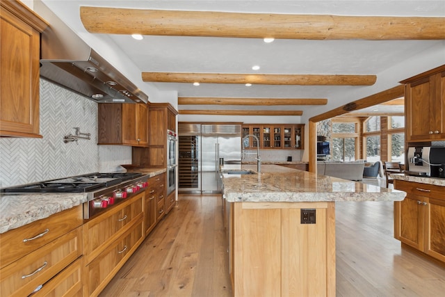 kitchen featuring backsplash, appliances with stainless steel finishes, beamed ceiling, and a center island with sink