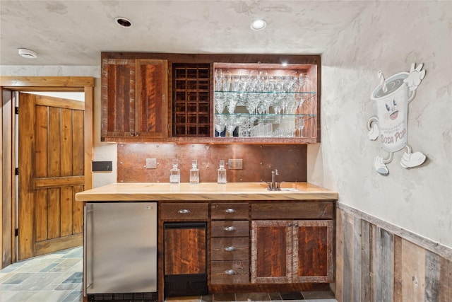 bar featuring sink, stainless steel refrigerator, and wood walls