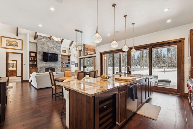 kitchen with light stone countertops, pendant lighting, built in shelves, wine cooler, and an island with sink