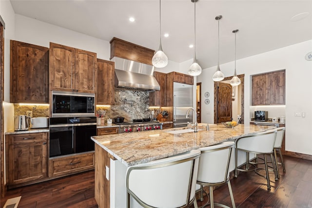 kitchen with black appliances, wall chimney exhaust hood, sink, backsplash, and a kitchen island with sink