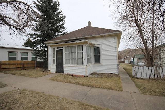 view of front of house with a shingled roof, fence, and a chimney