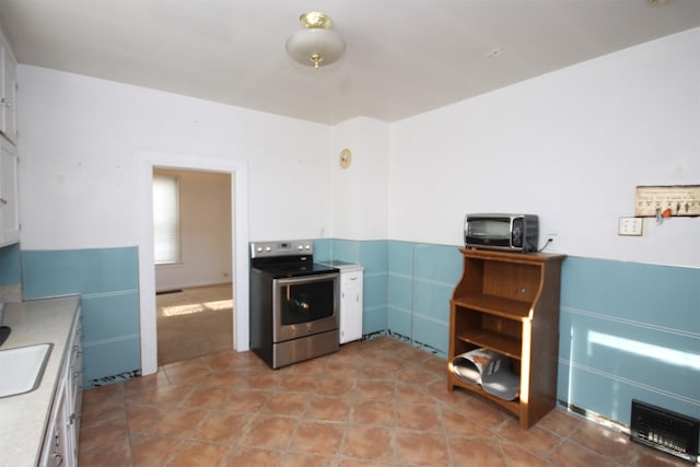 kitchen featuring a toaster, stainless steel electric range, a sink, light countertops, and white cabinets