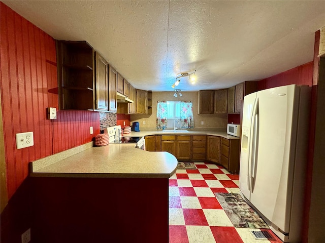 kitchen with white appliances, rail lighting, kitchen peninsula, a textured ceiling, and sink