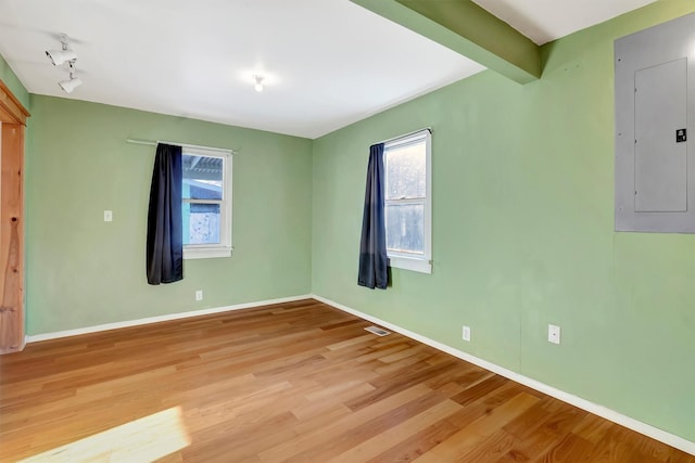 empty room with track lighting, electric panel, beam ceiling, and light hardwood / wood-style flooring