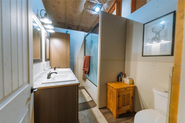 bathroom with combined bath / shower with glass door, toilet, vanity, and wood finished floors