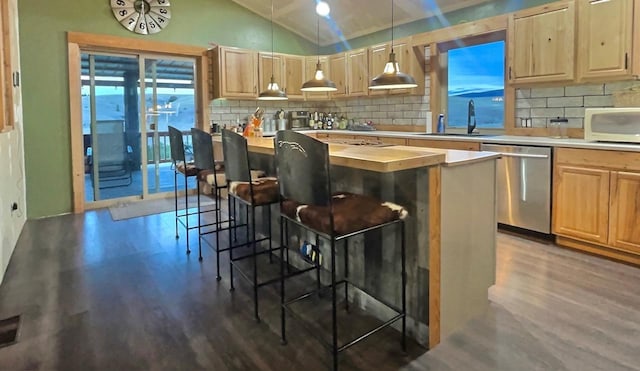 kitchen featuring decorative light fixtures, stainless steel dishwasher, white microwave, light brown cabinets, and vaulted ceiling