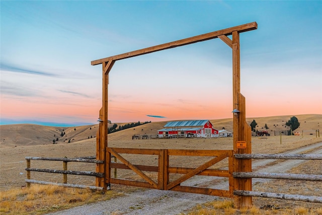 view of gate with a barn, a rural view, fence, and a mountain view