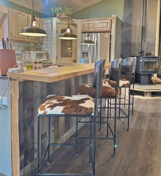 bar with backsplash, wood finished floors, stainless steel fridge, lofted ceiling, and a wood stove