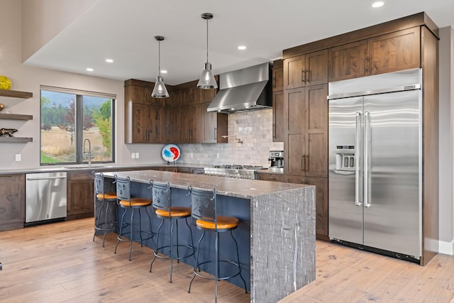 kitchen featuring stone counters, a kitchen island, sink, stainless steel appliances, and wall chimney exhaust hood