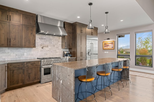 kitchen featuring premium appliances, backsplash, a kitchen island, wall chimney exhaust hood, and light stone counters