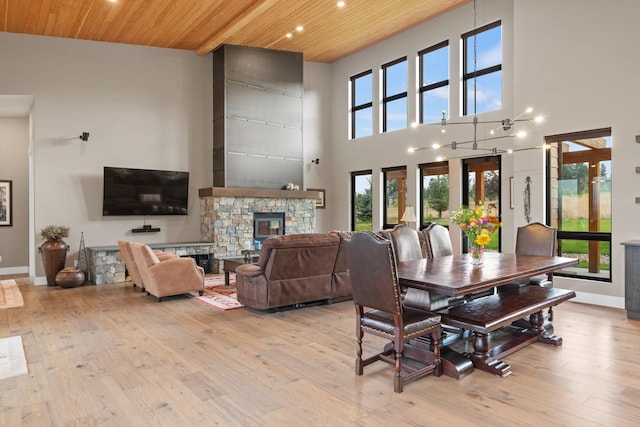 dining room with a high ceiling, a stone fireplace, light hardwood / wood-style floors, and wooden ceiling