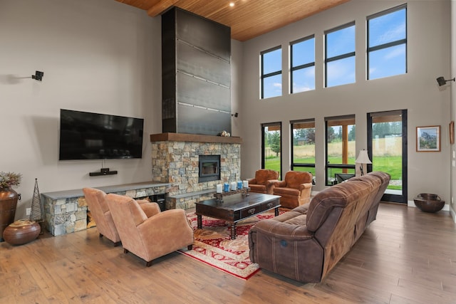 living room featuring a high ceiling, a stone fireplace, wood ceiling, and light wood-type flooring