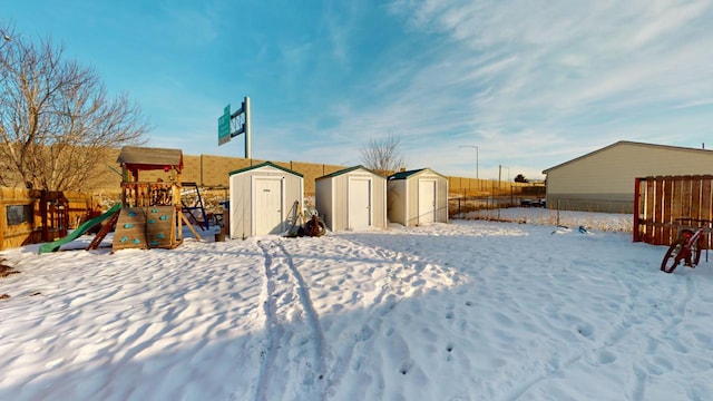 yard covered in snow featuring a playground and a storage shed