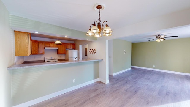 kitchen with kitchen peninsula, white appliances, pendant lighting, ceiling fan with notable chandelier, and light hardwood / wood-style flooring