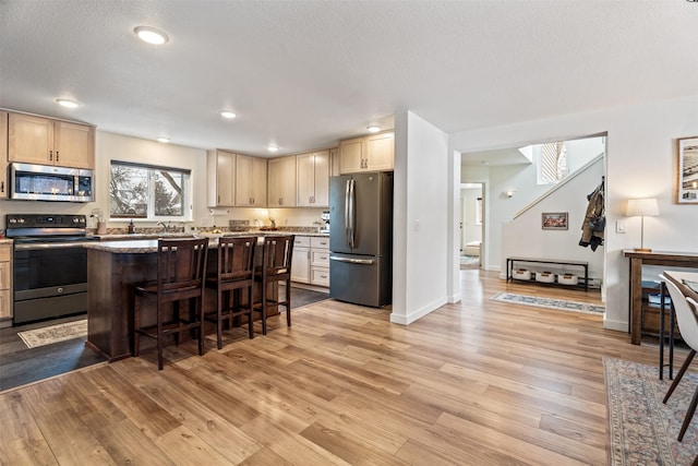 kitchen featuring light stone countertops, a kitchen island, a kitchen bar, stainless steel appliances, and light wood-type flooring