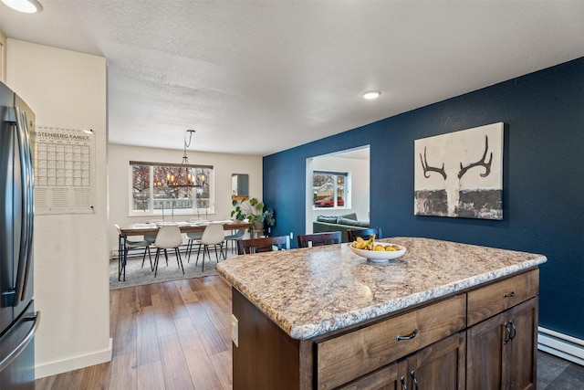 kitchen with baseboard heating, a kitchen island, dark hardwood / wood-style flooring, hanging light fixtures, and stainless steel refrigerator