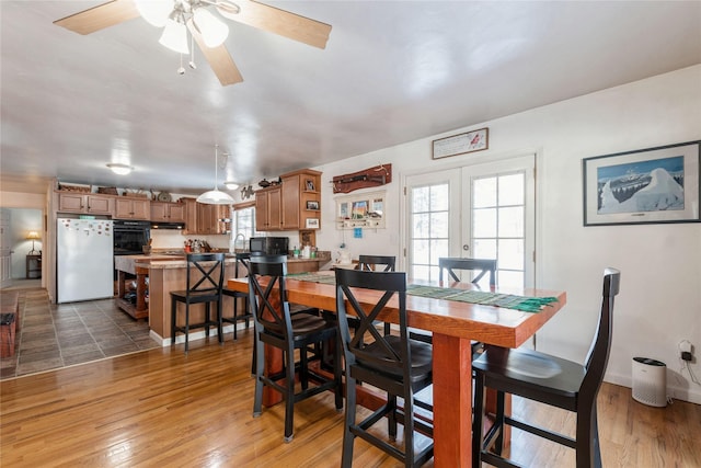 dining area with healthy amount of natural light, a ceiling fan, wood finished floors, and french doors