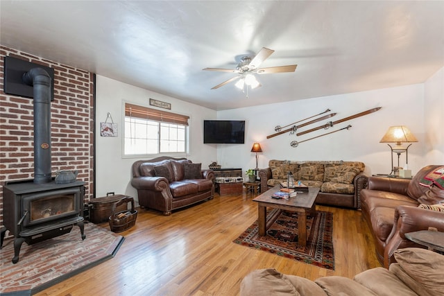 living room with a wood stove, a ceiling fan, and hardwood / wood-style flooring