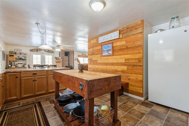 kitchen featuring ceiling fan, white fridge, kitchen peninsula, wooden walls, and a wood stove