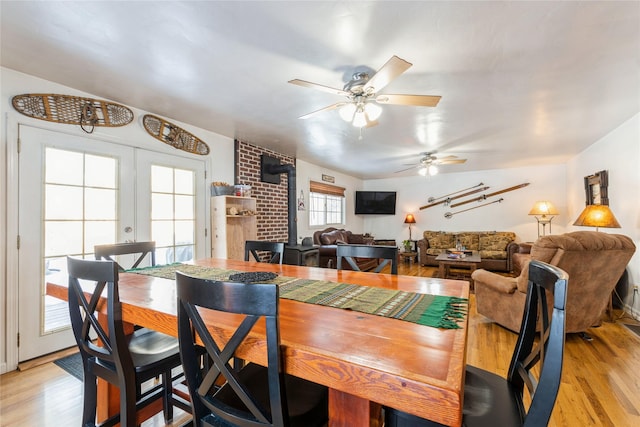 dining space with a wood stove, a ceiling fan, light wood-style floors, and french doors
