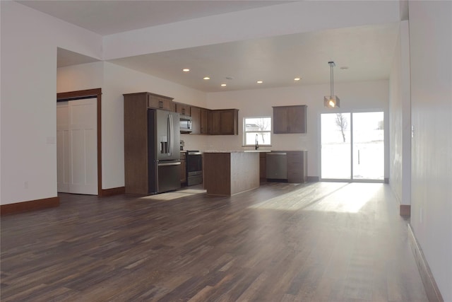 kitchen with dark hardwood / wood-style floors, pendant lighting, a kitchen island, sink, and stainless steel appliances