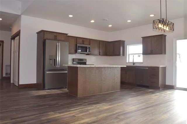 kitchen with pendant lighting, appliances with stainless steel finishes, a center island, dark hardwood / wood-style flooring, and dark brown cabinets