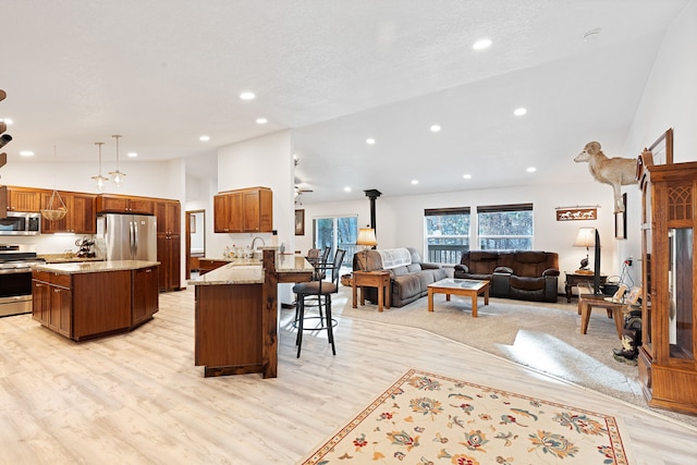 kitchen with appliances with stainless steel finishes, light hardwood / wood-style floors, sink, hanging light fixtures, and a breakfast bar