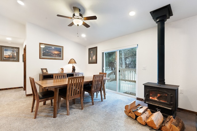 carpeted dining area featuring ceiling fan, vaulted ceiling, and a wood stove