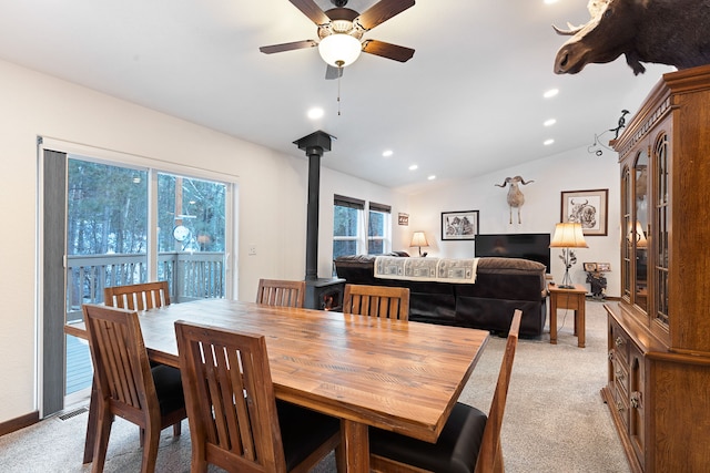 dining room featuring vaulted ceiling, light carpet, a wood stove, and ceiling fan