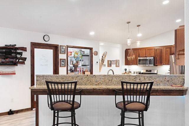 kitchen featuring light hardwood / wood-style floors, pendant lighting, appliances with stainless steel finishes, a breakfast bar area, and light stone counters