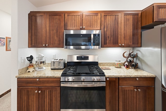 kitchen with light stone counters, appliances with stainless steel finishes, and vaulted ceiling