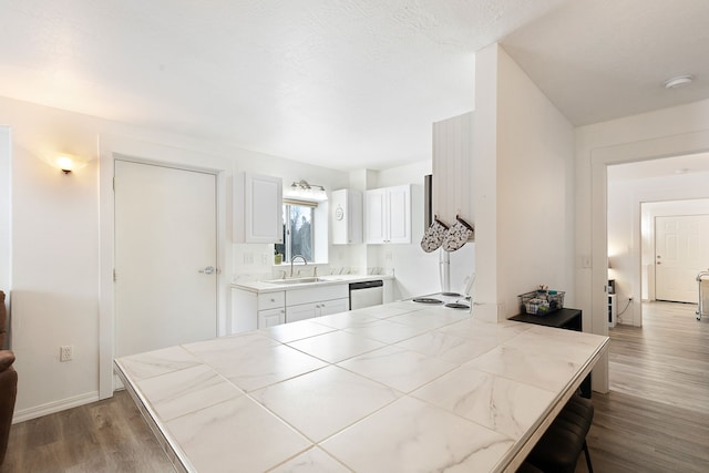 kitchen with tile countertops, wood-type flooring, stainless steel dishwasher, white cabinets, and sink