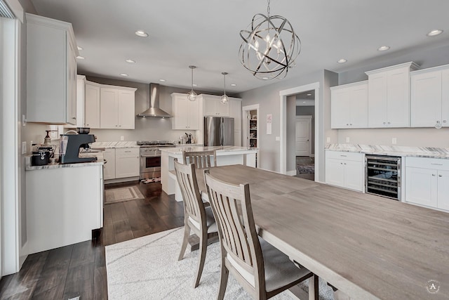 kitchen with pendant lighting, beverage cooler, a center island, appliances with stainless steel finishes, and wall chimney range hood