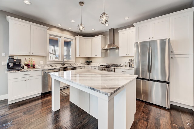 kitchen featuring stainless steel appliances, wall chimney range hood, hanging light fixtures, light stone countertops, and a center island