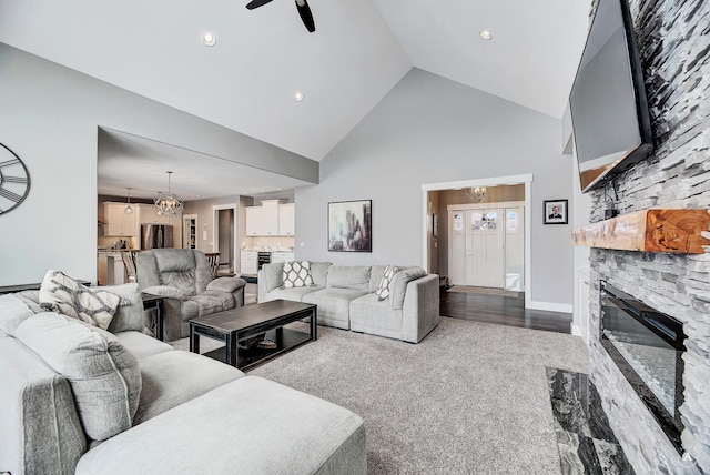 carpeted living room with high vaulted ceiling, ceiling fan with notable chandelier, and a stone fireplace