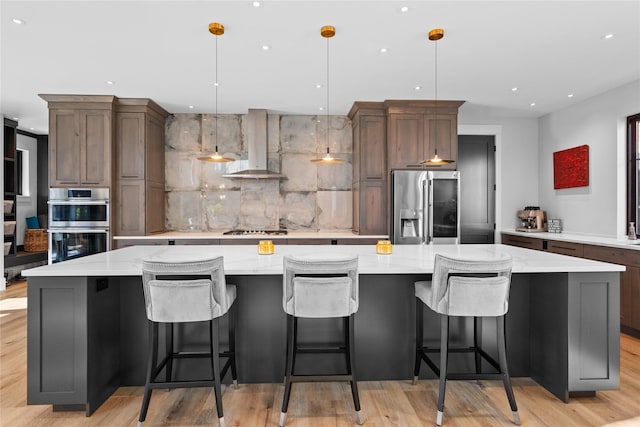 kitchen with appliances with stainless steel finishes, a breakfast bar area, hanging light fixtures, a large island, and wall chimney exhaust hood