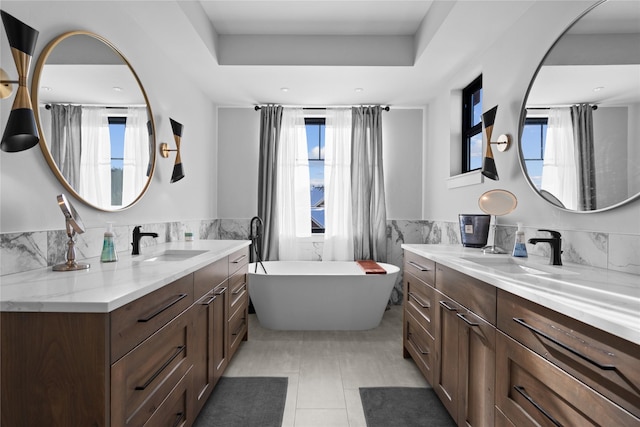 bathroom with vanity, a raised ceiling, a bathtub, and tile walls