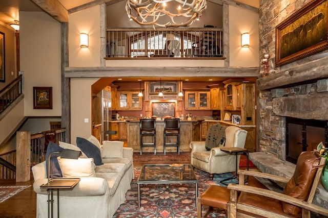 living room featuring an inviting chandelier, a stone fireplace, hardwood / wood-style flooring, and a high ceiling