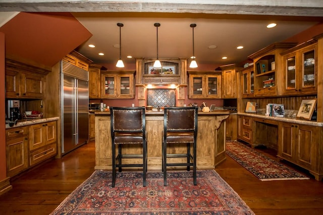 kitchen with light stone counters, hanging light fixtures, dark hardwood / wood-style floors, a kitchen breakfast bar, and built in fridge