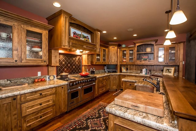 kitchen featuring dark hardwood / wood-style floors, tasteful backsplash, range with two ovens, hanging light fixtures, and light stone counters