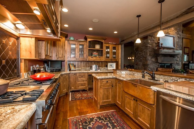 kitchen featuring appliances with stainless steel finishes, dark hardwood / wood-style floors, a fireplace, decorative light fixtures, and light stone countertops