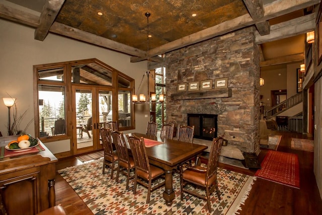 dining room with french doors, wood-type flooring, a stone fireplace, and beam ceiling