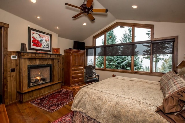 bedroom featuring multiple windows, a tiled fireplace, wood-type flooring, and ceiling fan