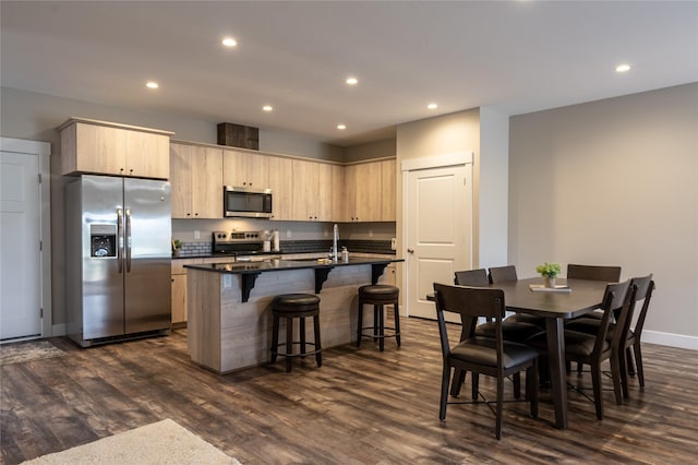 kitchen featuring light brown cabinetry, dark hardwood / wood-style floors, stainless steel appliances, and a kitchen island with sink