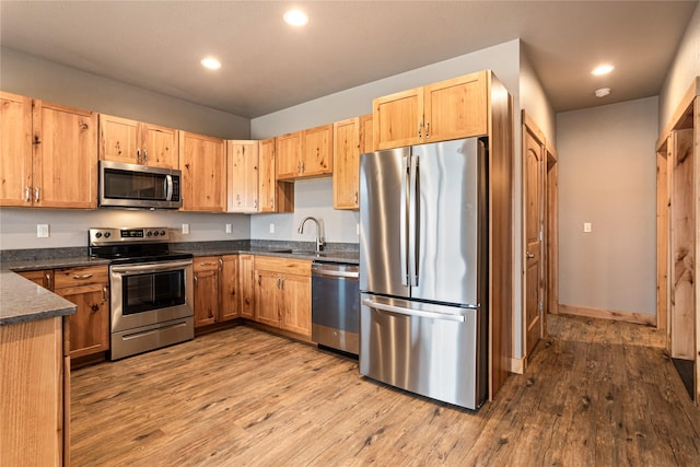 kitchen featuring recessed lighting, stainless steel appliances, a sink, dark countertops, and wood finished floors