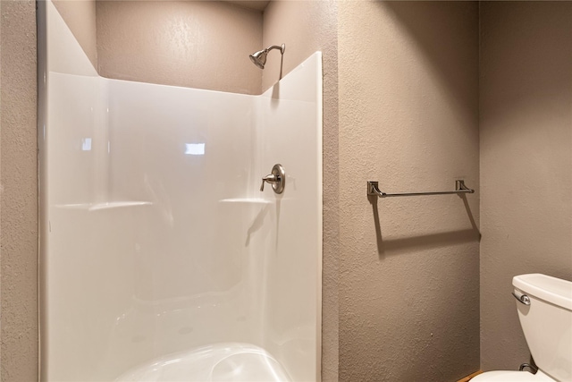 full bath featuring a textured wall, toilet, and a stall shower