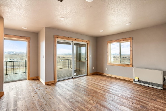 spare room featuring heating unit, baseboards, wood finished floors, and a textured ceiling
