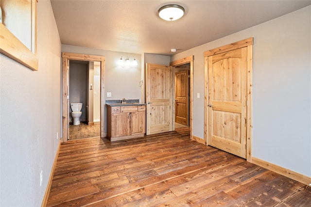 unfurnished bedroom featuring a sink, ensuite bath, dark wood-style floors, and baseboards