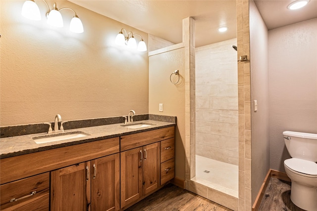 bathroom with toilet, a tile shower, hardwood / wood-style floors, and vanity